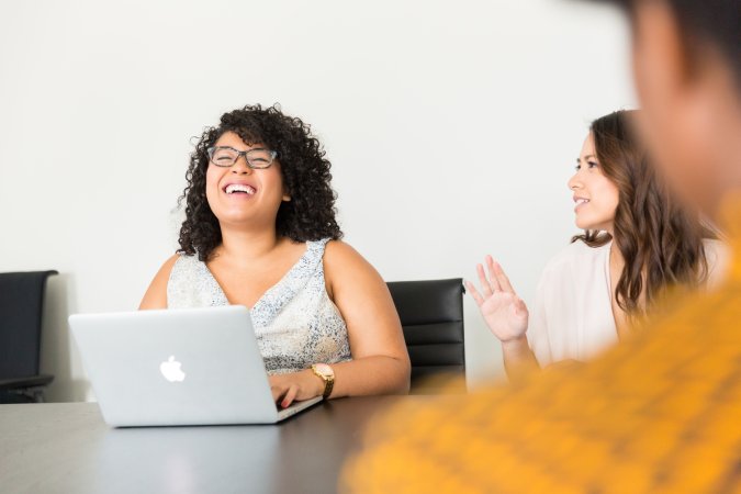 a woman at a conference room table with an Apple Mac laptop, in a meeting