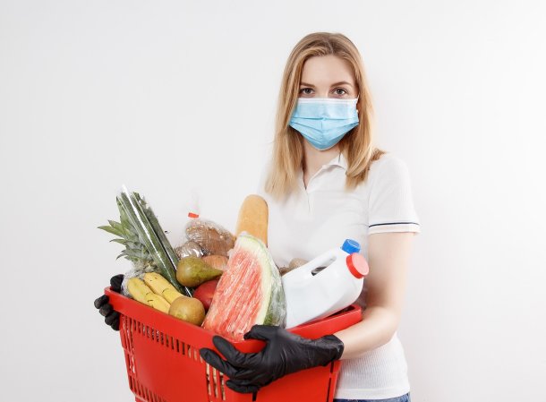 Person in a mask and disposable gloves holding a basket of groceries