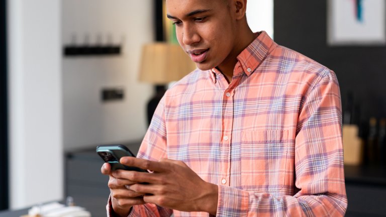 A young man wearing an orange plaid shirt focusing intently on an iPhone he's holding in front of him, as if he needs to make the keyboard bigger to see what he's typing.
