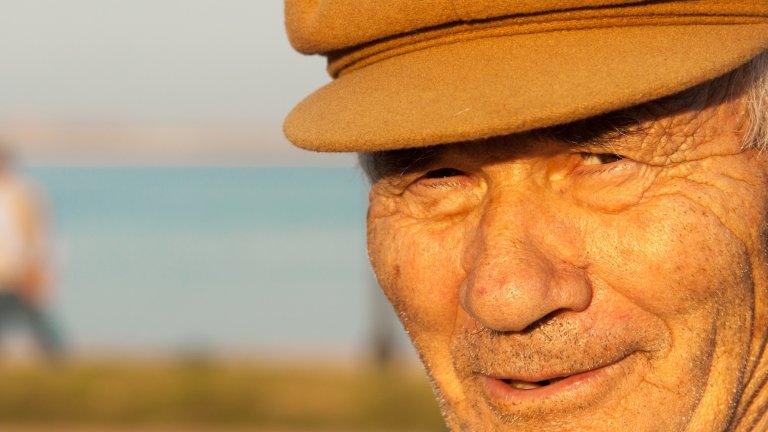 Sant'Antiocho, Sardinia, Italy - May 6, 2008: A senior fisherman in a traditional cap squints at the camera at golden hour with the sea in the background in the fishing village of Sant'Antiocho. Close-up shot.